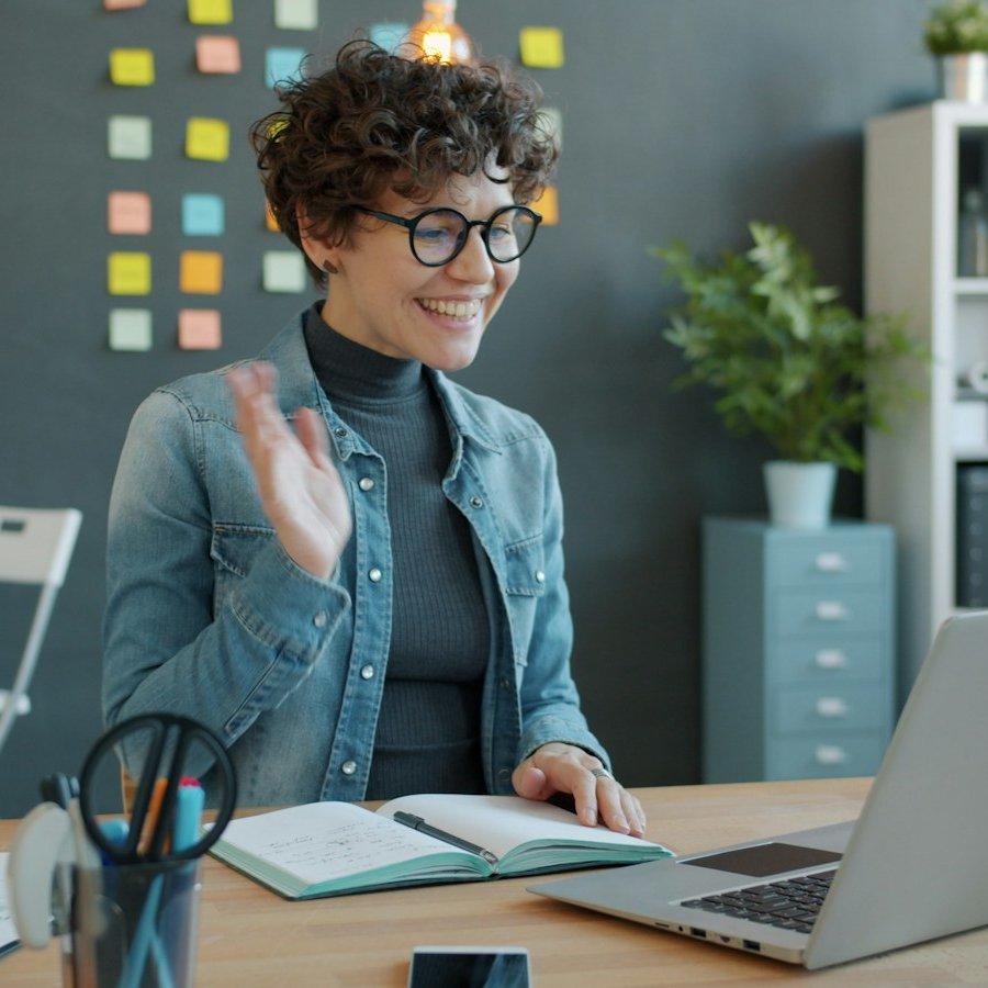 Smiling woman waving at her laptop during a video call